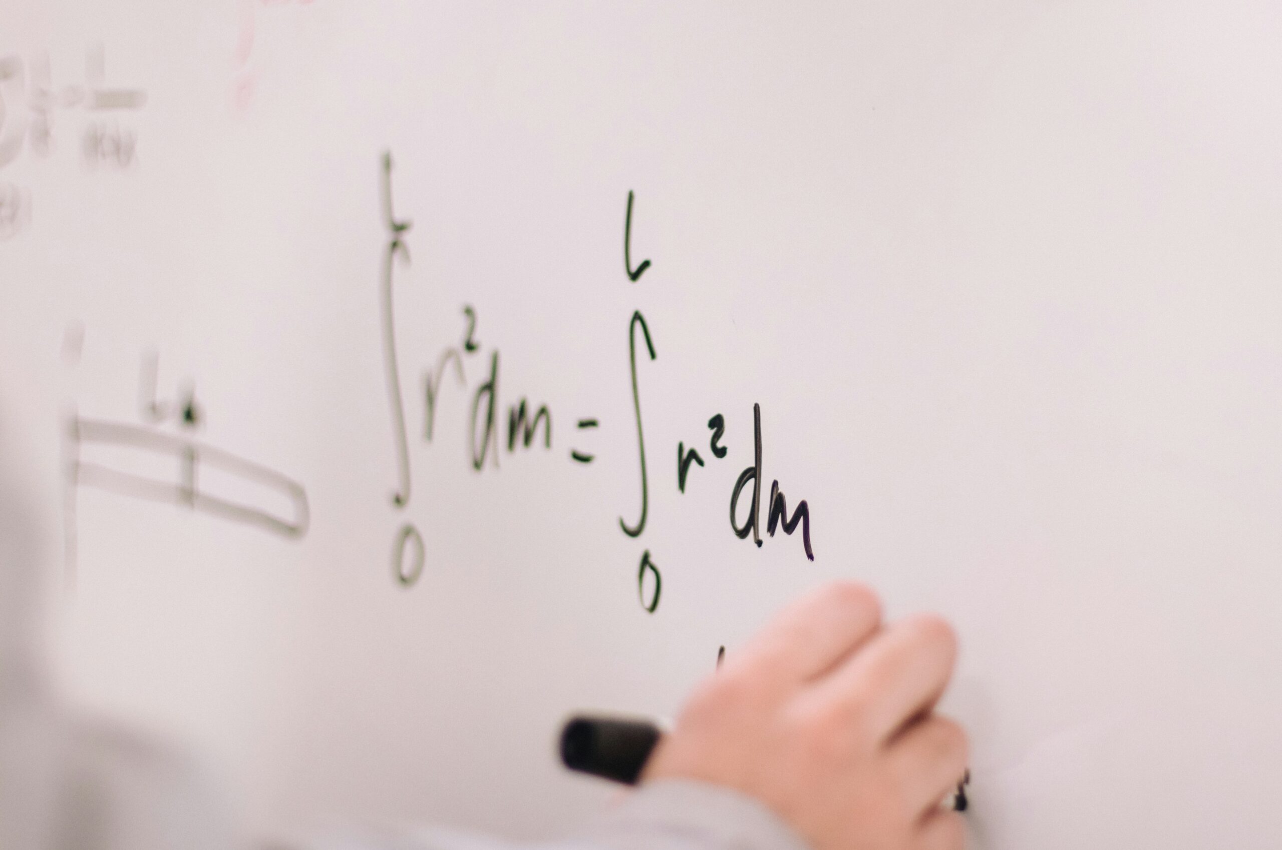 A close-up of a student's hand writing calculus equations on a whiteboard, featuring integral notation.