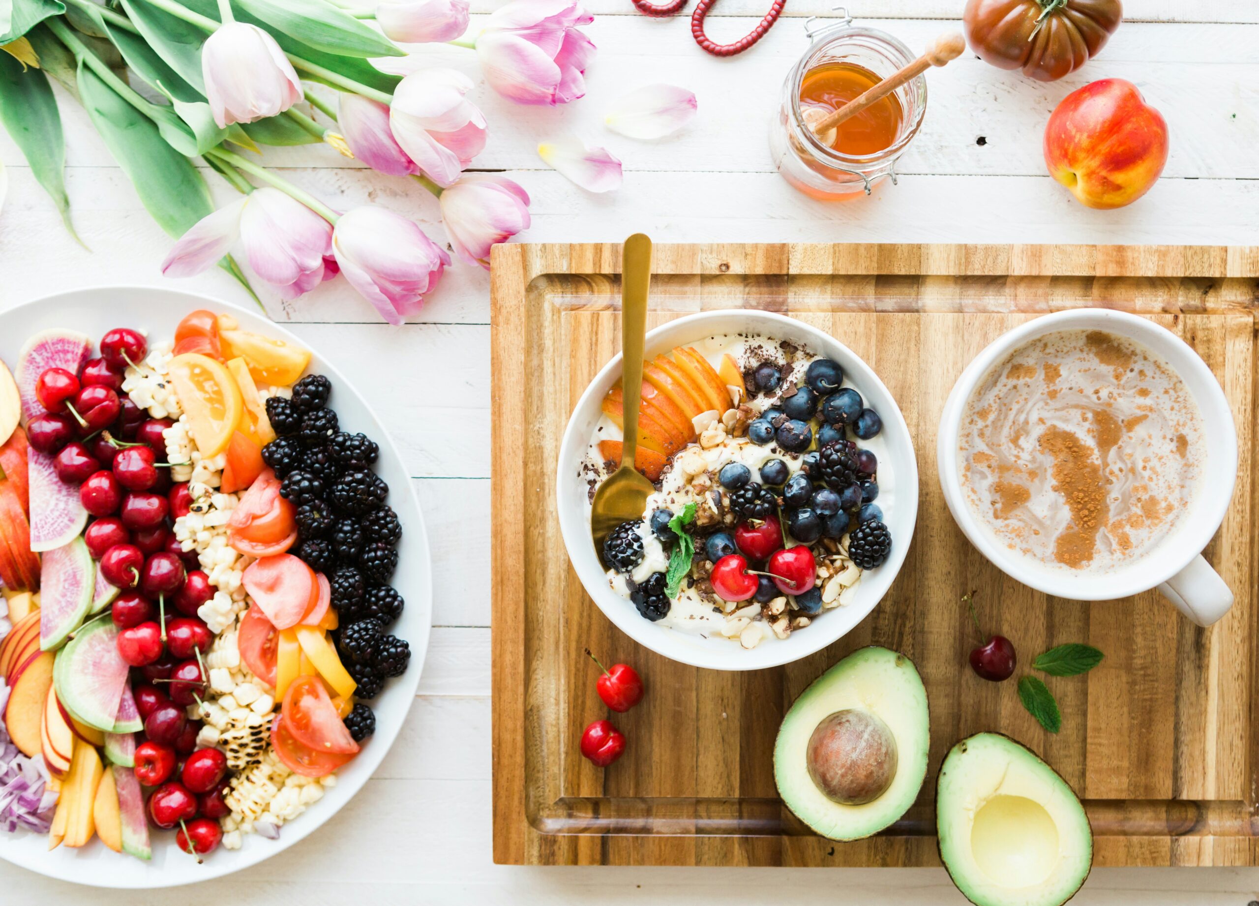 A healthy assortment of brain-boosting foods, including fruits, yoghurt, avocado, and a cup of coffee, arranged on a wooden board.