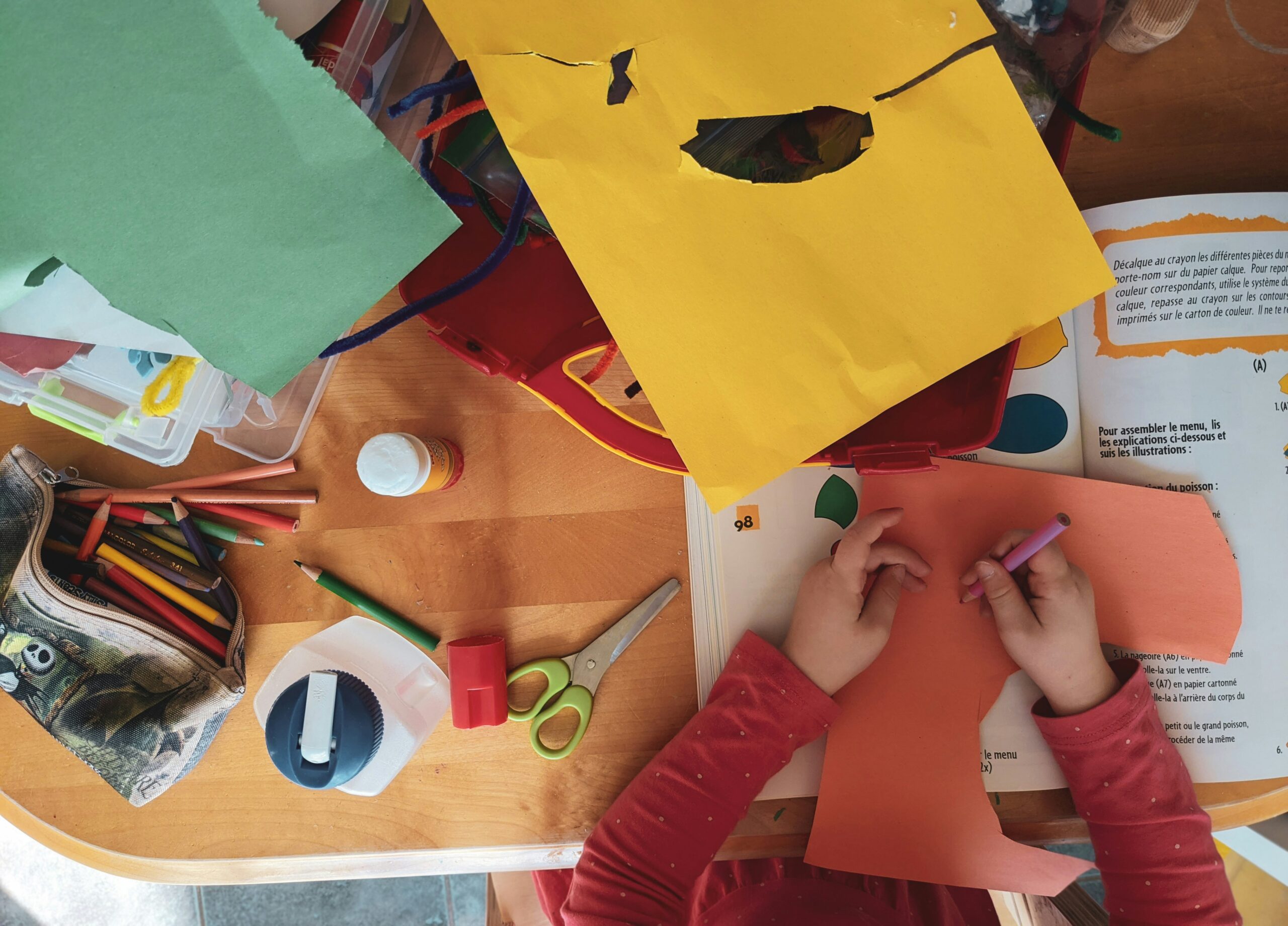 A child engaging in a hands-on learning activity with colorful paper, pencils, and scissors on a wooden desk.