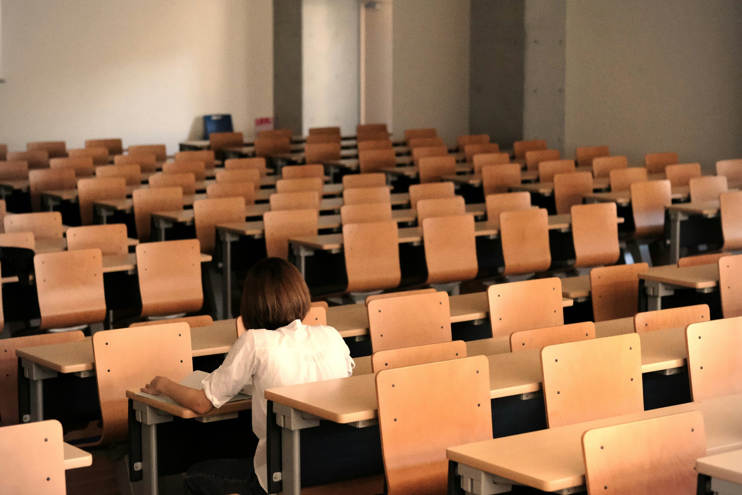 Student sitting alone among rows of empty desks, revising notes before a VCE SAC.