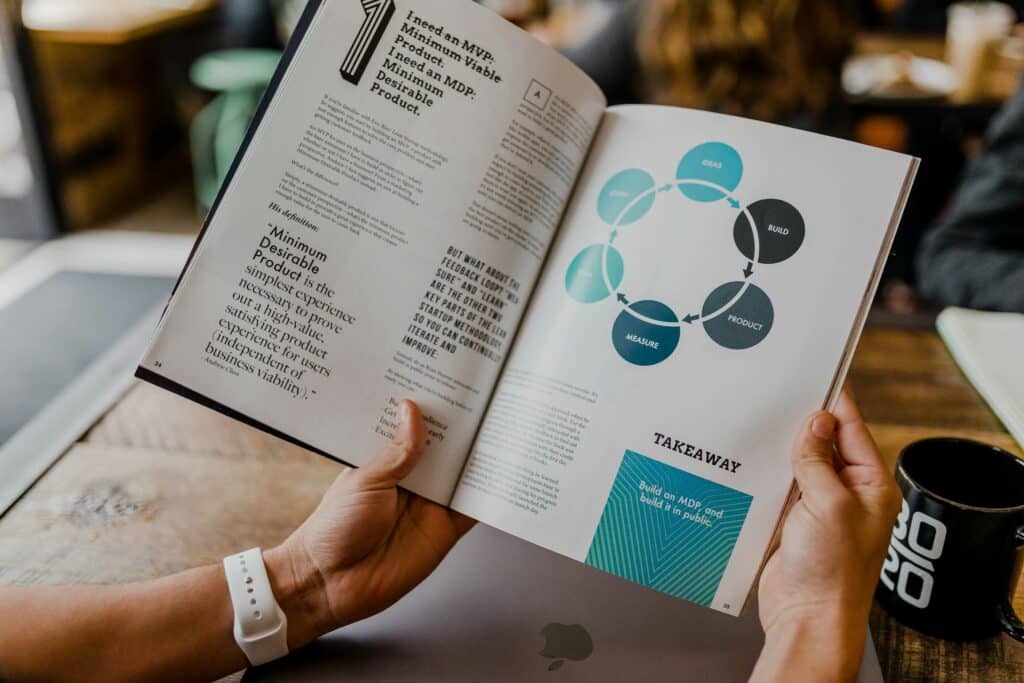 Person reading a business management book with diagrams and text on startup product development.