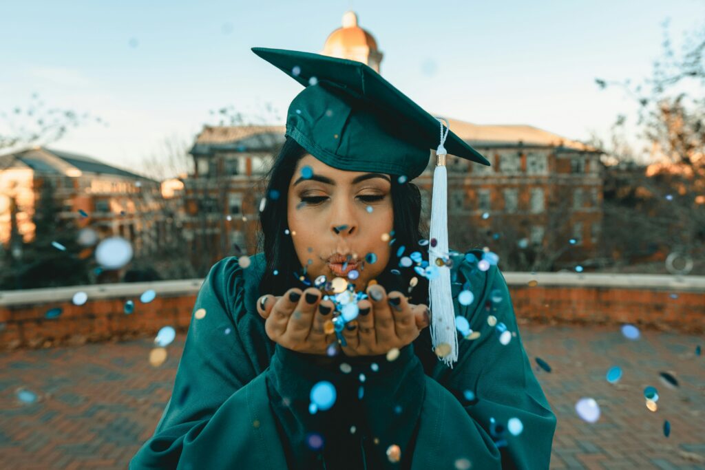 A graduate in a cap and gown blowing confetti, celebrating academic success and graduation.