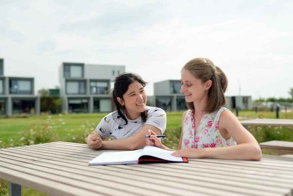 A tutor and student sitting together at an outdoor table working through a notebook — representing the supportive role parents play in helping their child prepare for Year 12 and the ATAR
