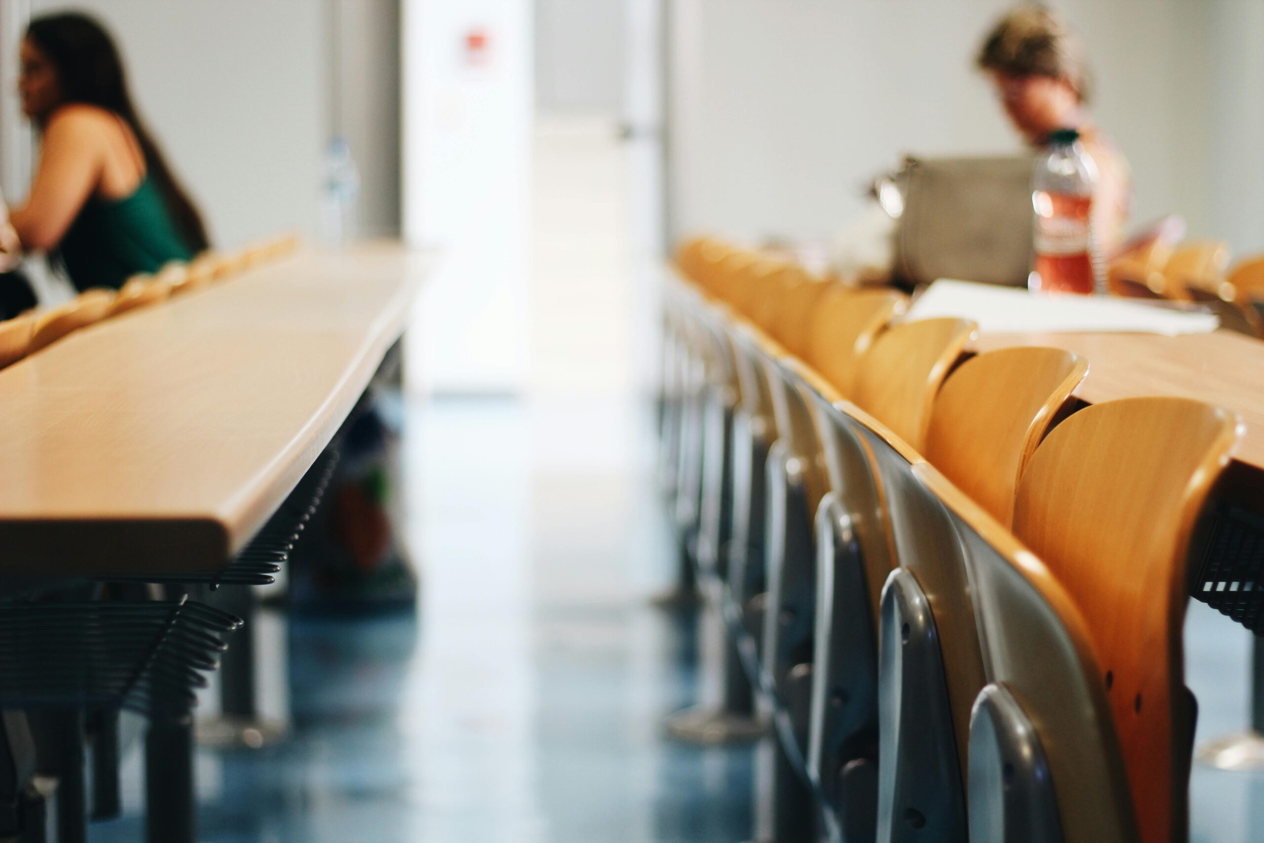 A quiet study space in a classroom with rows of empty chairs, with a student focused on their work in the background.