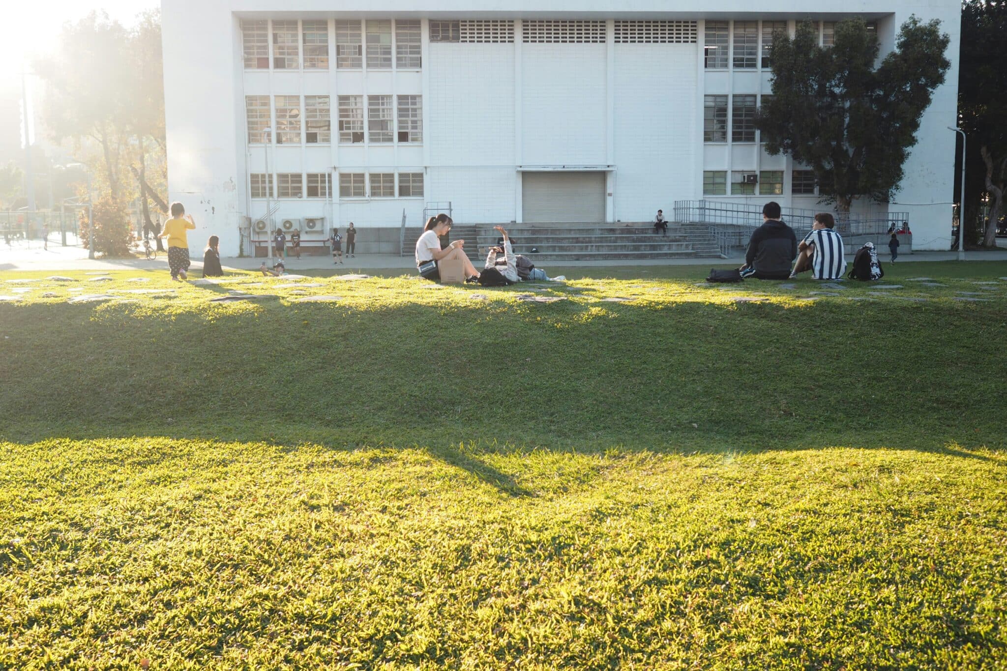Students sitting and relaxing on a grassy school campus in the afternoon light, representing rest, social connection and balance during Queensland school holiday periods.